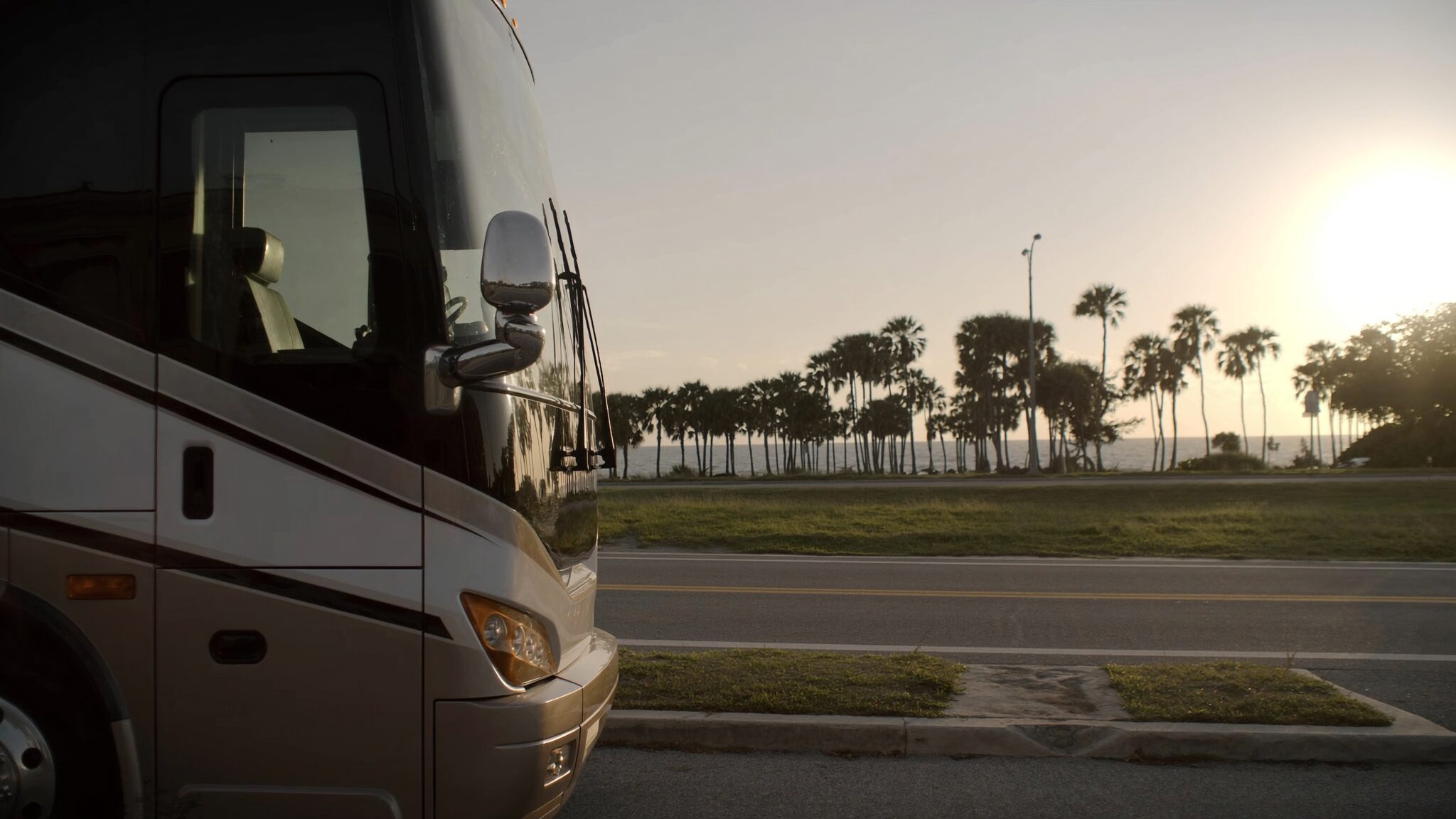 A luxury motorcoach beside a palm-lined Florida coastal road at golden hour